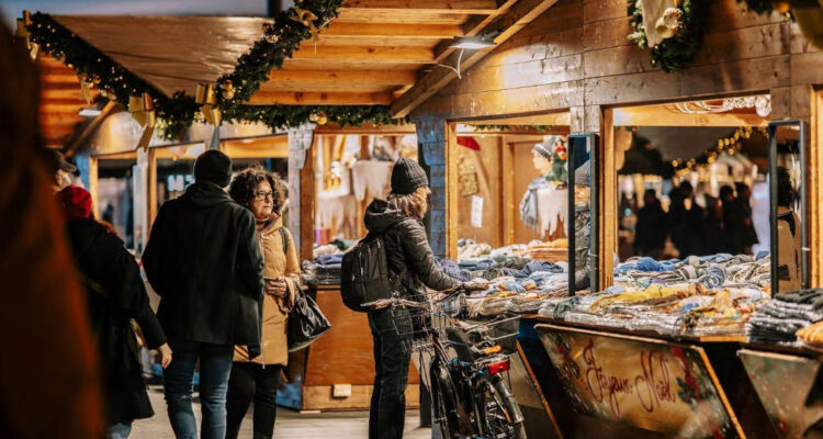 alcune persone tra le casette in legno illuminate di un mercatino di natale