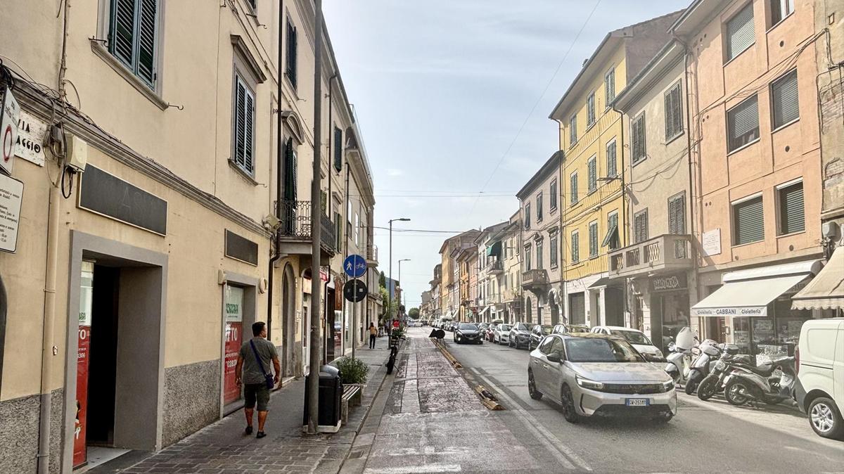 Via Primo Maggio a Pontedera, asse commerciale con vetrine e traffico, tra chiusure di negozi