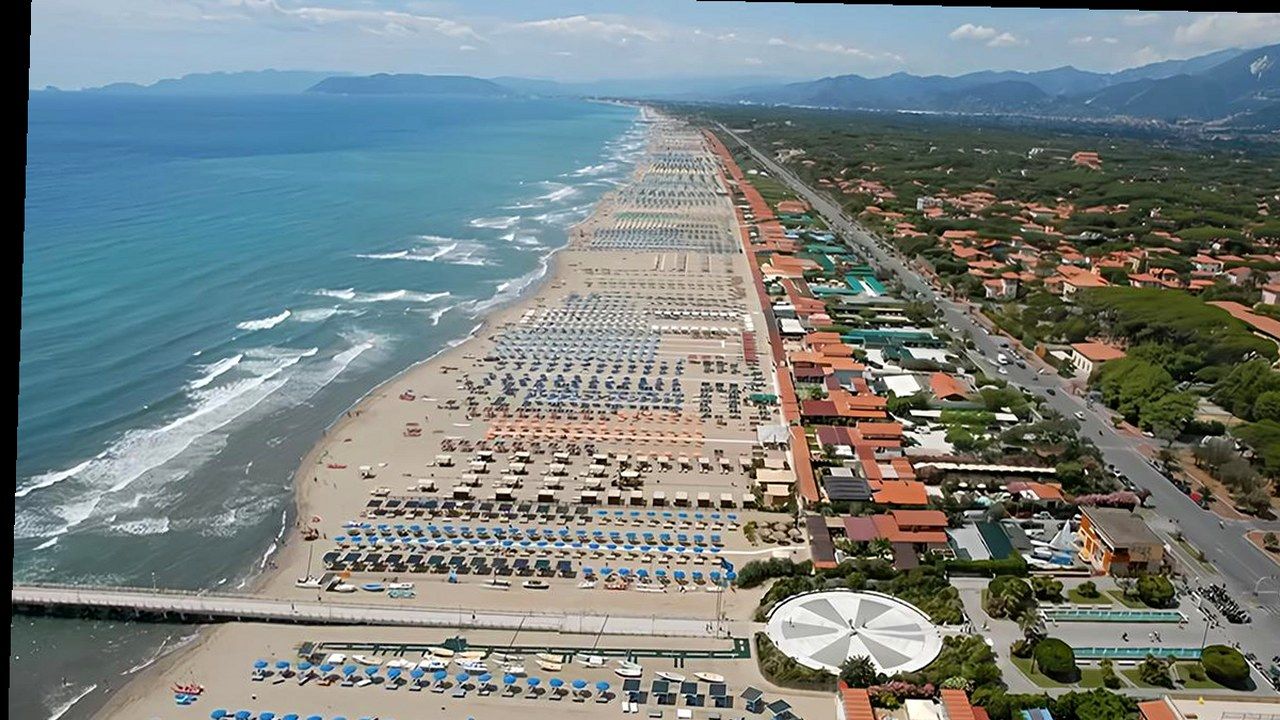 Veduta aerea di una spiaggia della Versilia con file di ombrelloni, lungomare e Alpi Apuane sullo sfondo
