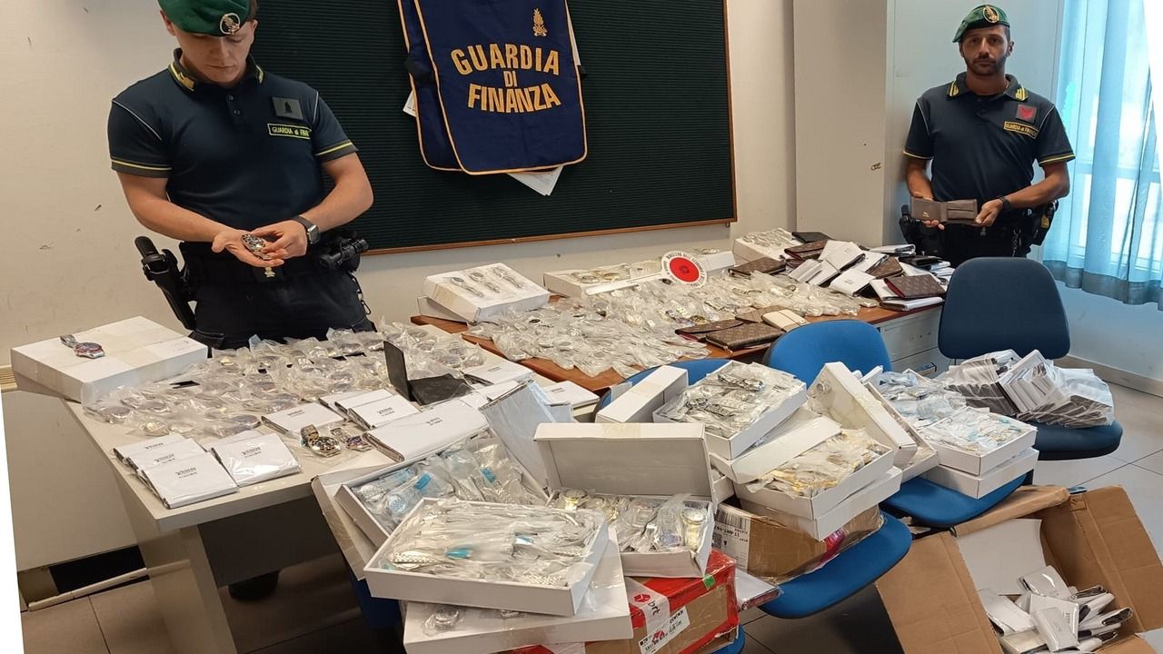Due finanzieri mostrano orologi Rolex falsi e portafogli sequestrati in un ufficio della Guardia di Finanza a Pisa