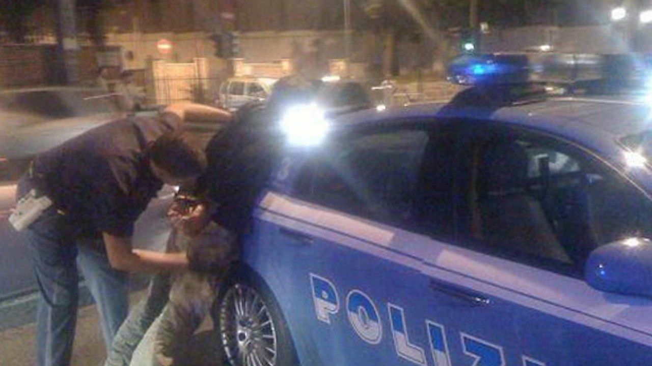 Arresto della Polizia di Stato: agente ferma un uomo accanto a una volante con lampeggianti accesi