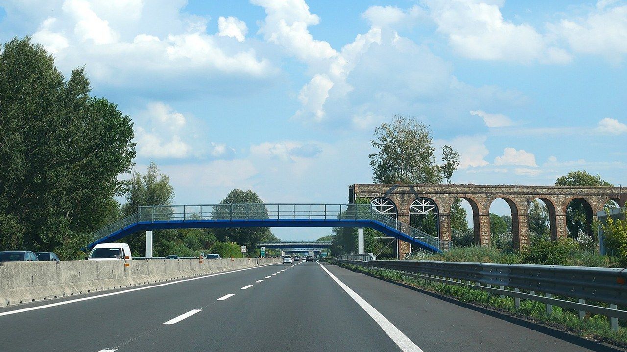 L'autostrada A11 alle porte di Lucca, con il guardrail lungo la carreggiata e l'acquedotto del Nottolini sullo sfondo (foto Naioli, Wikimedia Commons, CC BY-SA 4.0)
