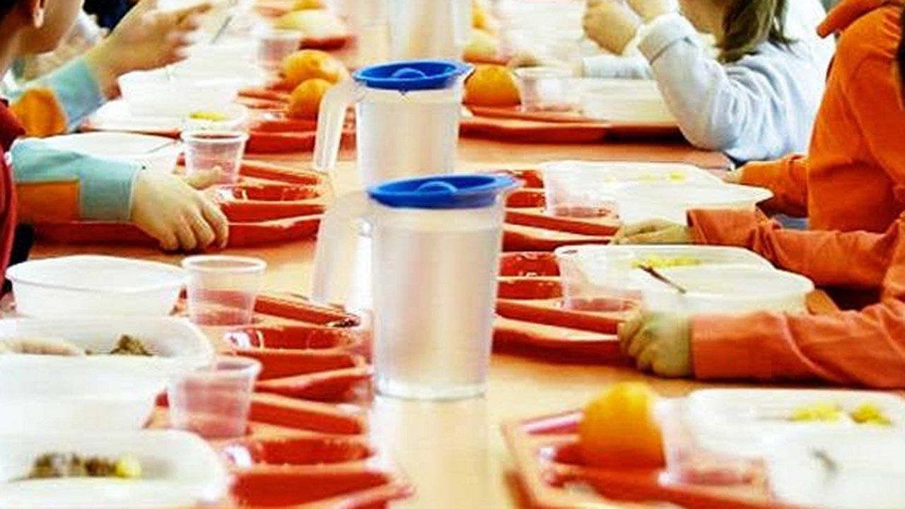 Bambini a mensa scolastica con vassoi e caraffe d’acqua sui banchi