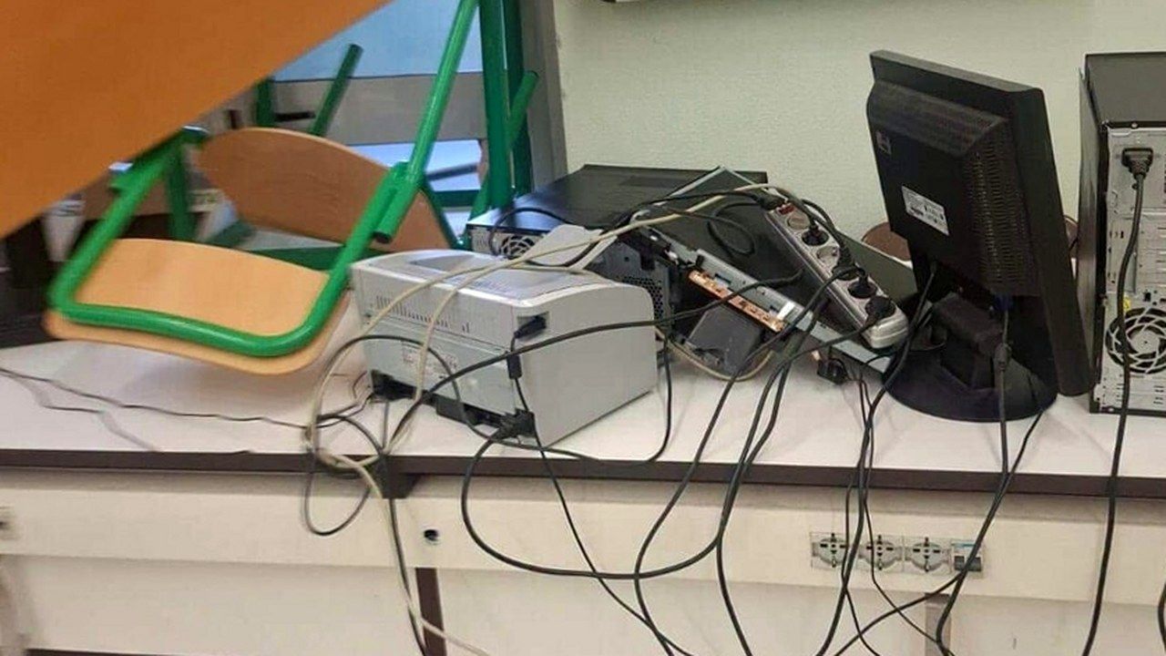 Aula del Pacinotti di Pisa dopo l'occupazione: computer, stampante e cavi ammassati sul banco, sedie rovesciate