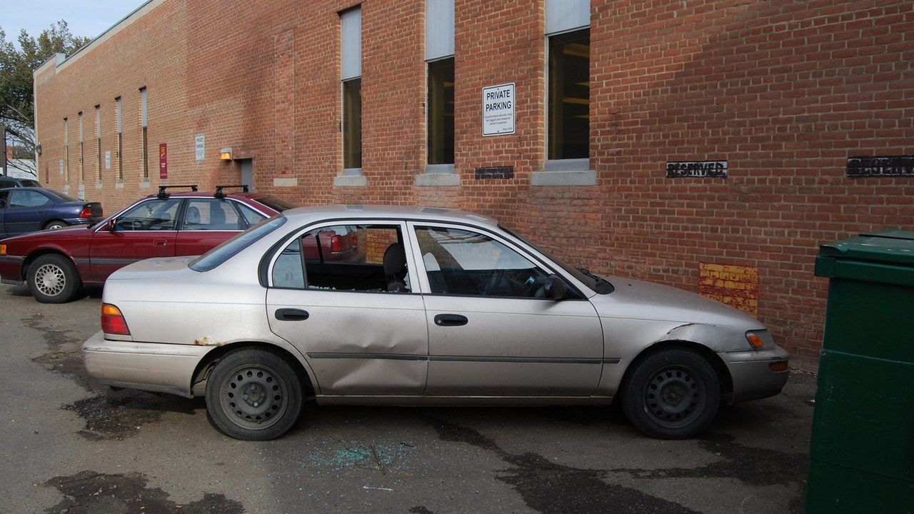 Auto con il finestrino laterale spaccato e vetri a terra in un parcheggio (foto d'archivio)