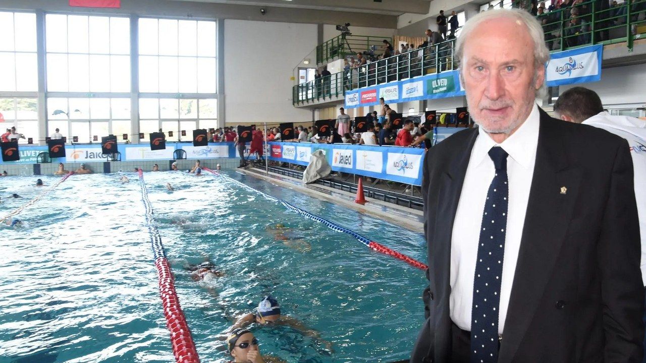 Una manifestazione di nuoto in piscina, con un uomo in giacca e cravatta a bordo vasca