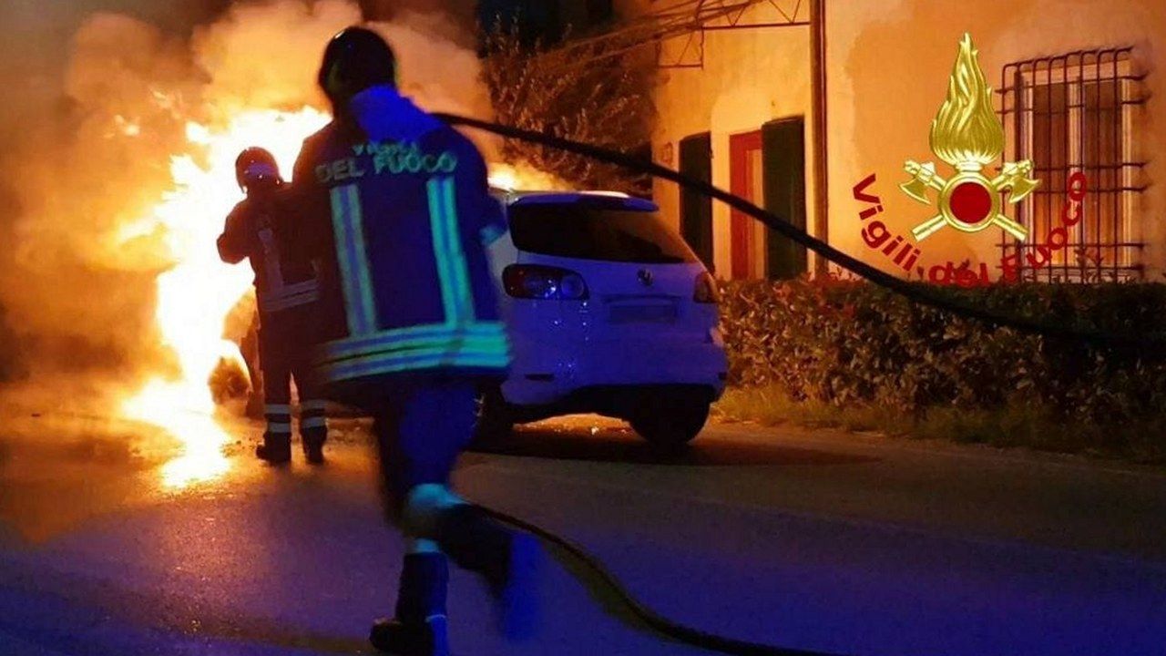 Vigili del Fuoco al lavoro di notte su un'auto in fiamme in strada, accanto alle abitazioni di Marlia