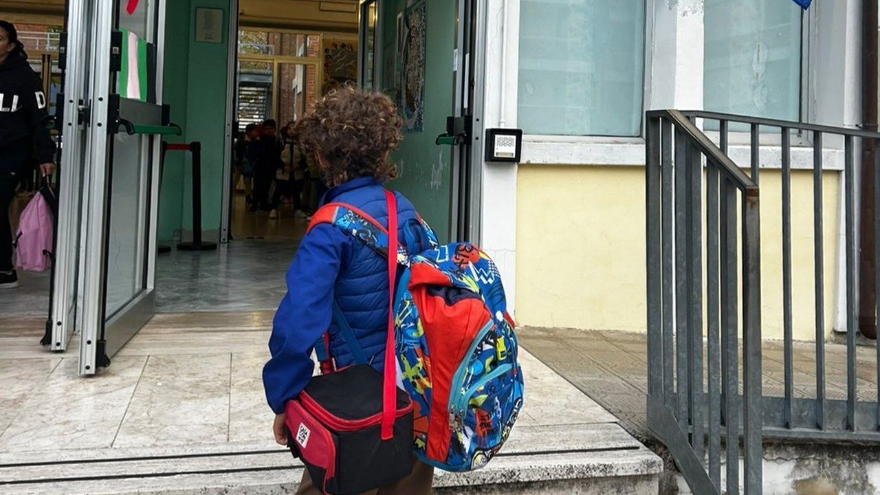 Un bambino con lo zaino e la borsa del pranzo sale le scale all'ingresso di una scuola di Viareggio