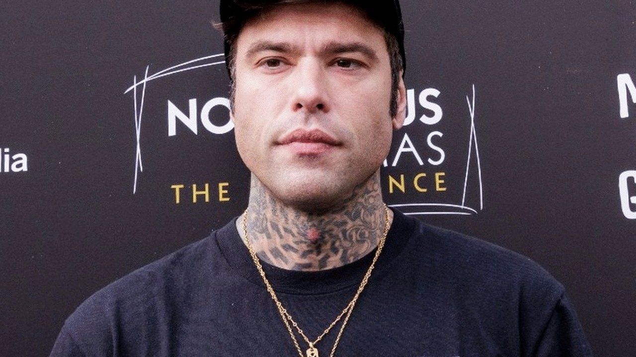 Fedez con il cappellino nero davanti a un pannello durante un evento pubblico